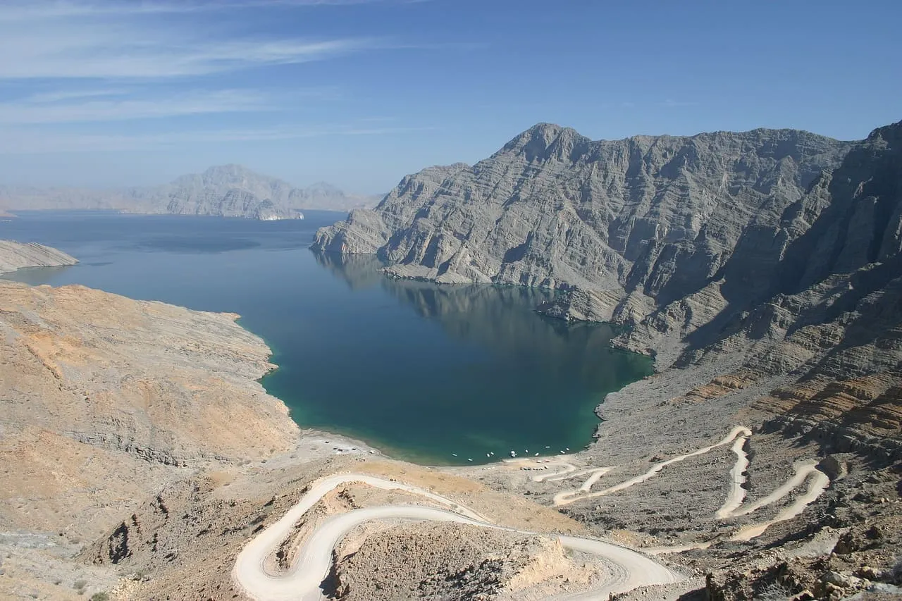 A gravel road winding down bare limestone mountains to the turquoise water of Khor Najd, a fjord near Khasab in Musandam