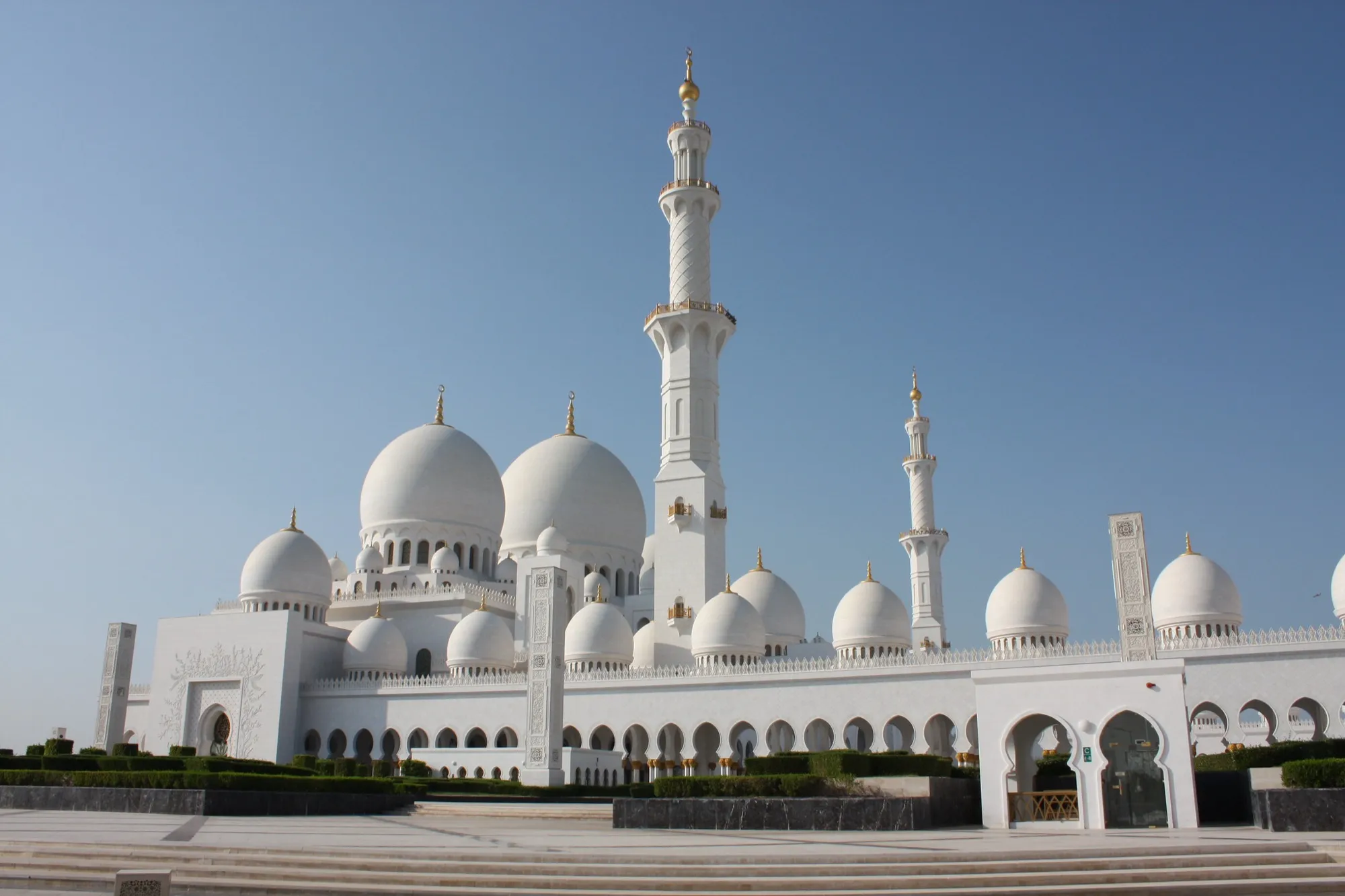 The white domes and minarets of the Sheikh Zayed Grand Mosque in Abu Dhabi under a clear sky