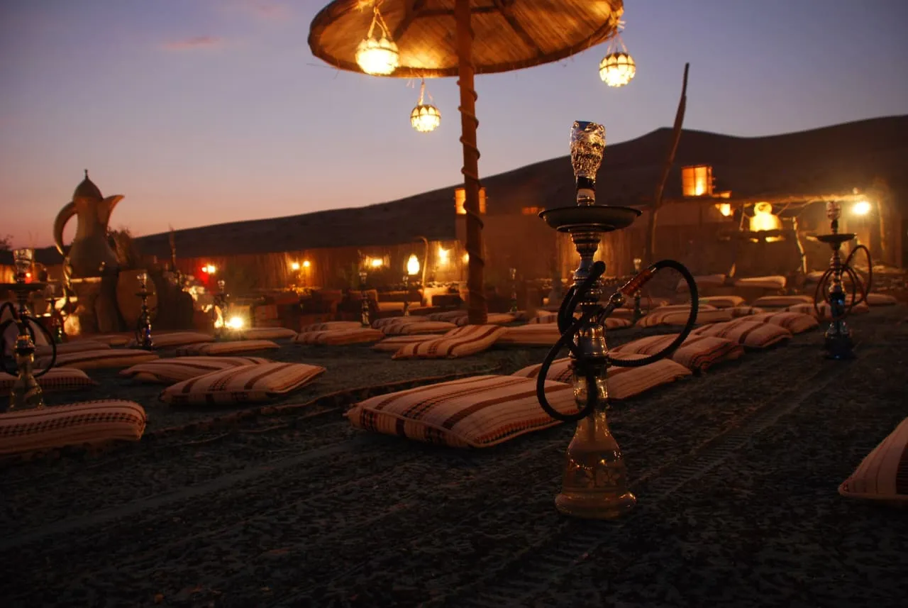 Floor cushions, lanterns and shisha pipes laid out on the sand at a Dubai desert camp at dusk