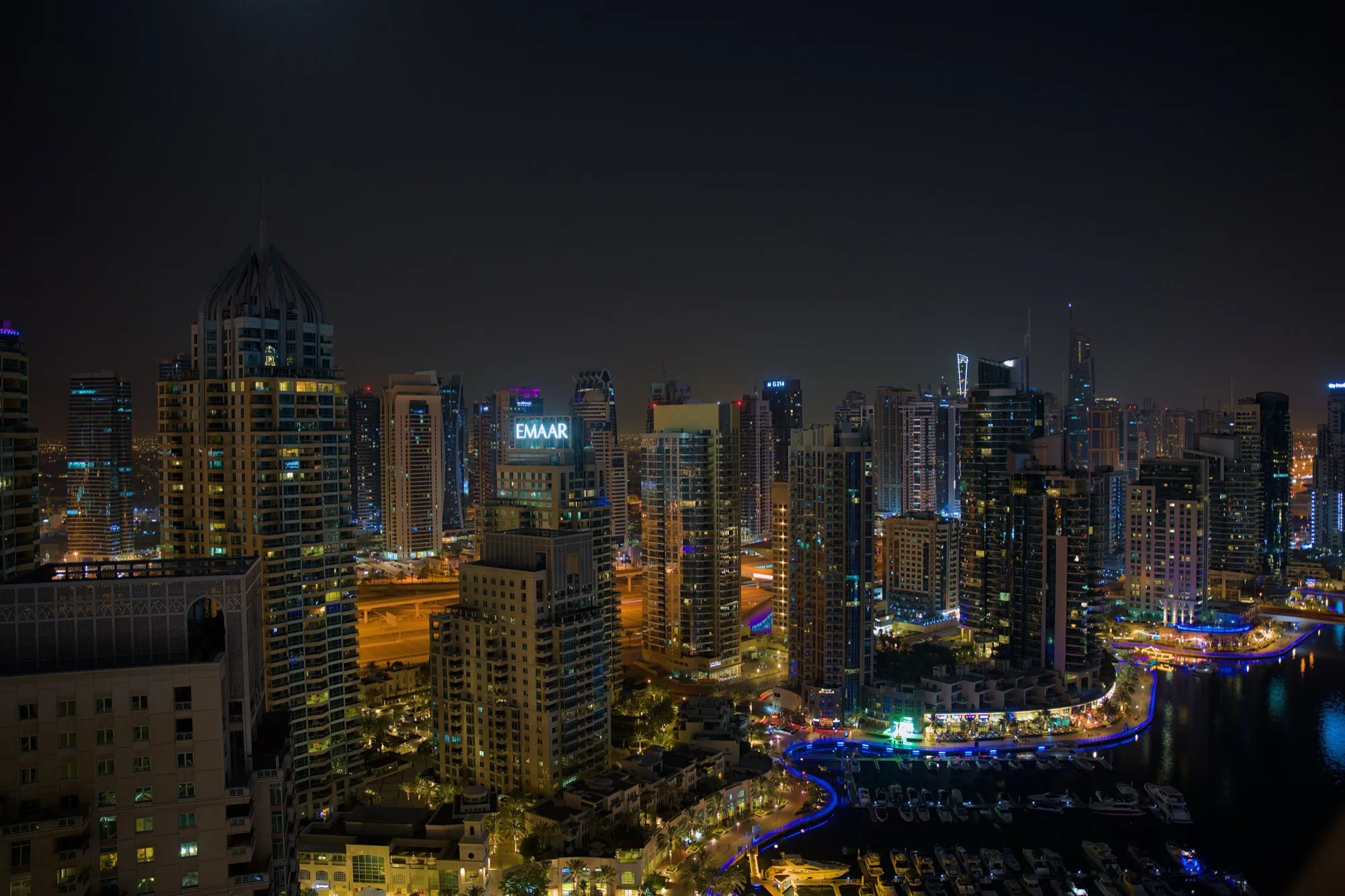 Dubai Marina at night from a high floor, with the lit promenade curving along the water