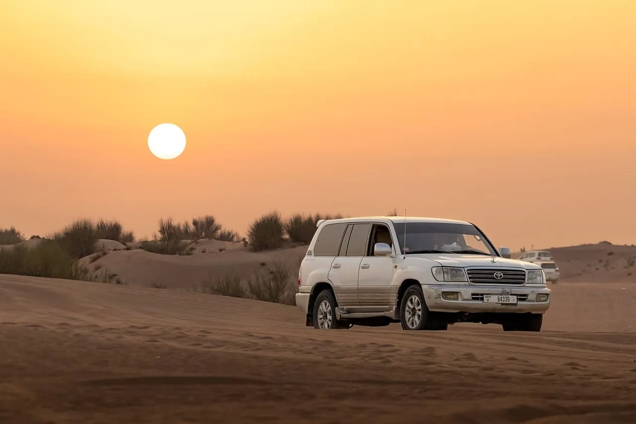A white Toyota Land Cruiser on the sand at sunset in the Dubai Desert Conservation Reserve