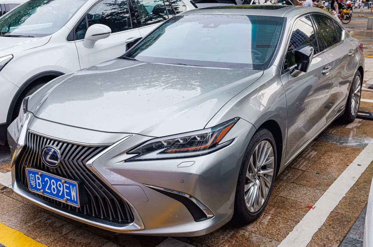 A silver Lexus ES 300h hybrid sedan parked on a wet street, seen from the front