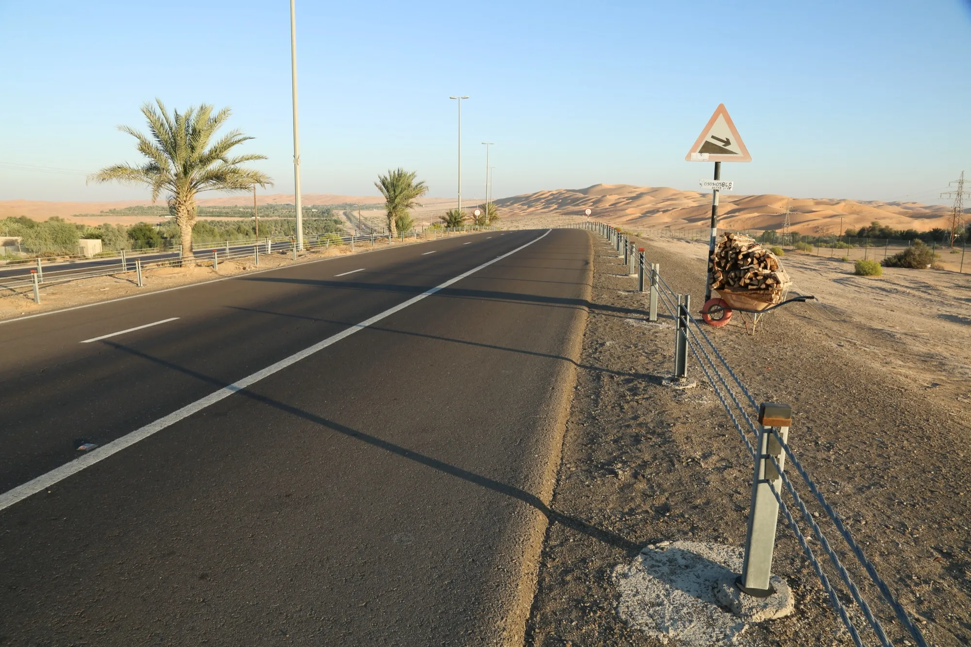 The road through Liwa, with date palms on one side and high sand dunes ahead