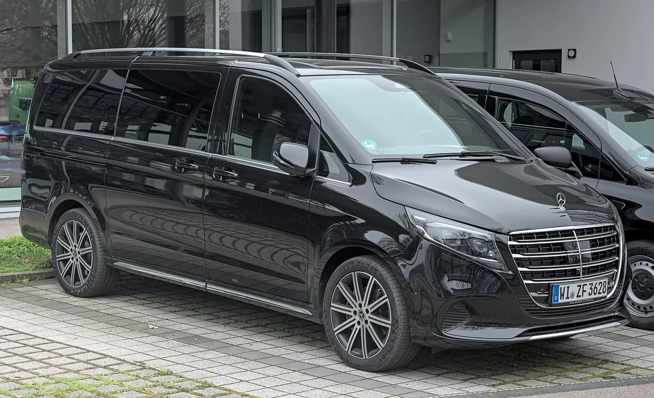 A black Mercedes-Benz V-Class van with tinted rear windows, parked outside a showroom