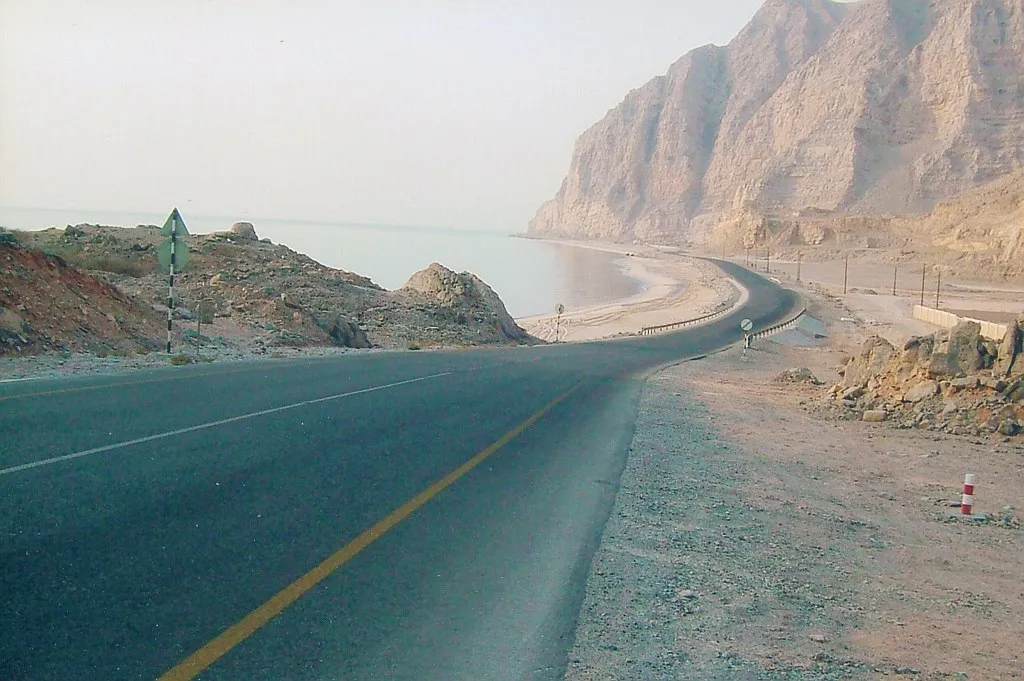 The coast road into Musandam after the UAE and Oman border, curving along the shore beneath sheer limestone cliffs on the way to Khasab
