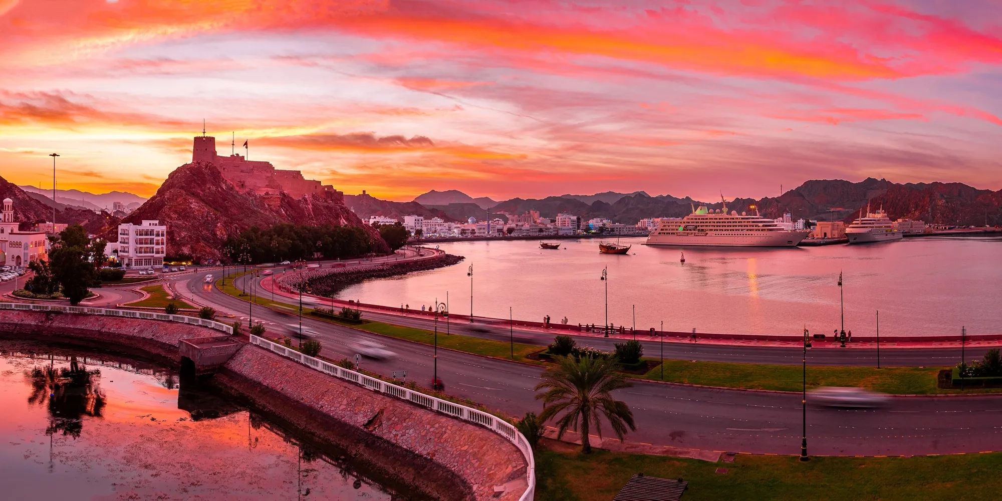 Muttrah Corniche and harbour in Muscat at sunset, with a hilltop fort above the bay