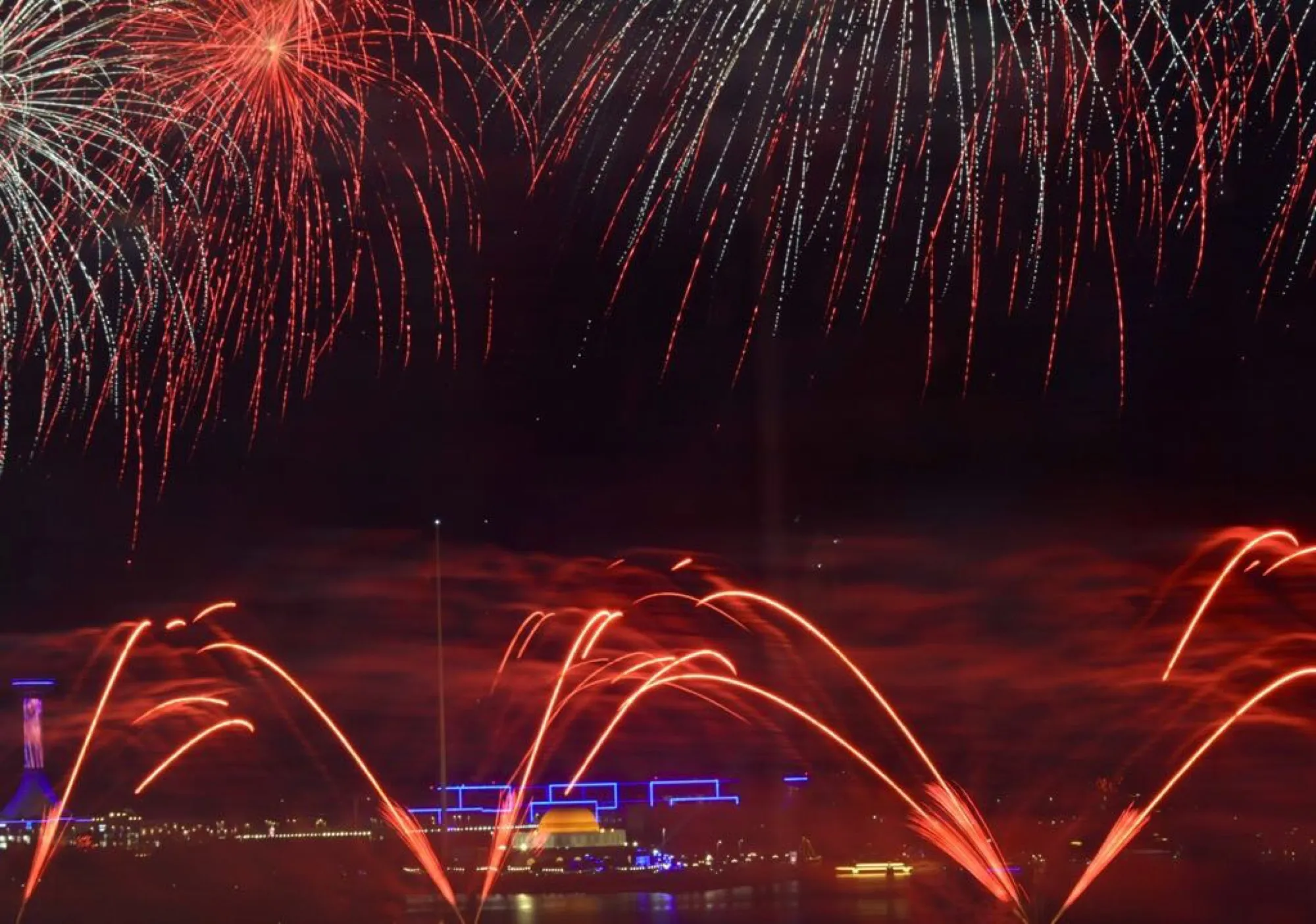 Red and white fireworks bursting over the water during UAE National Day celebrations