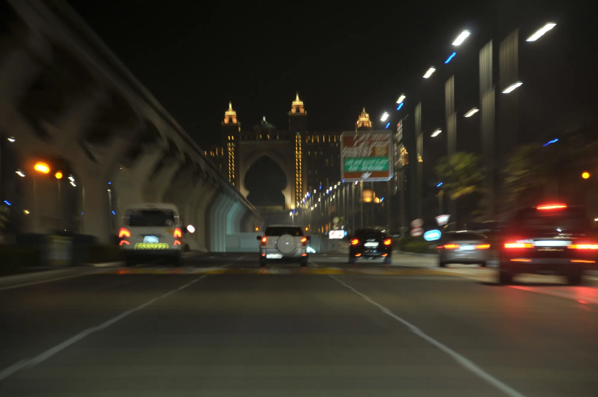 Evening traffic on the road along Palm Jumeirah, beside the monorail, with Atlantis The Palm lit up at the far end