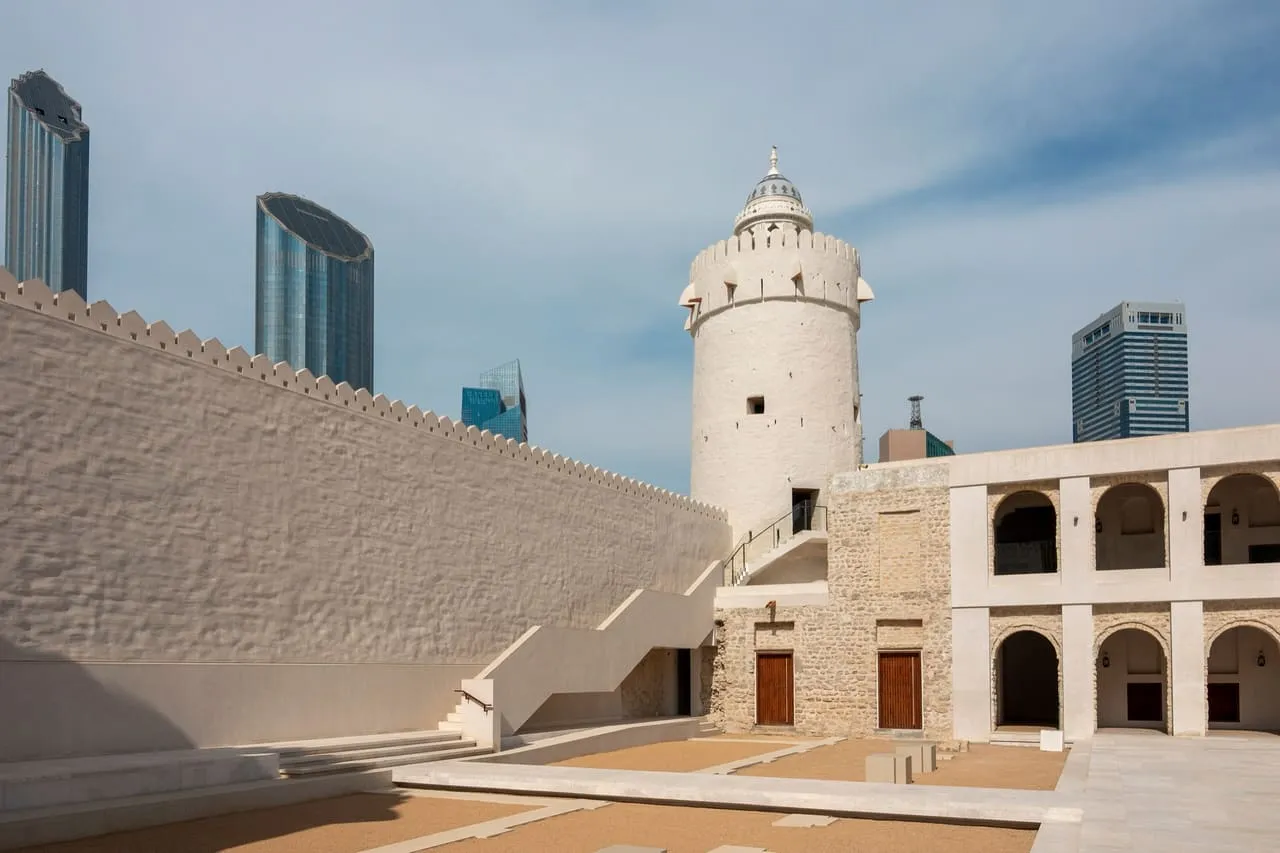The white watchtower and walls of Qasr Al Hosn, with city towers behind