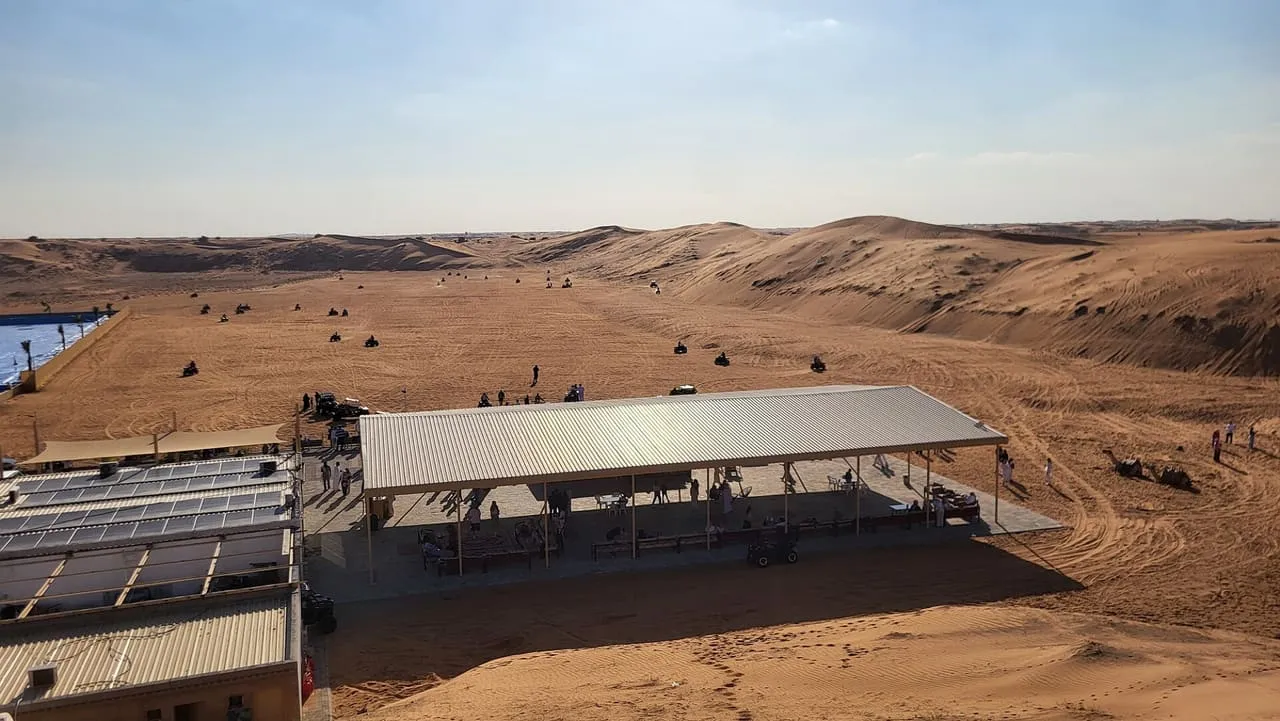 Quad bikes riding the open sand beside a shaded quad bike rental area in the desert of Dubai