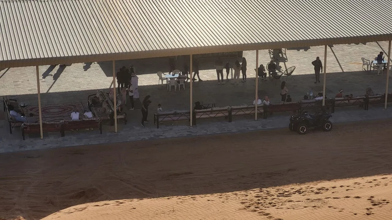 Riders waiting under the shade canopy at a quad bike base in the Dubai desert, with a quad parked on the sand
