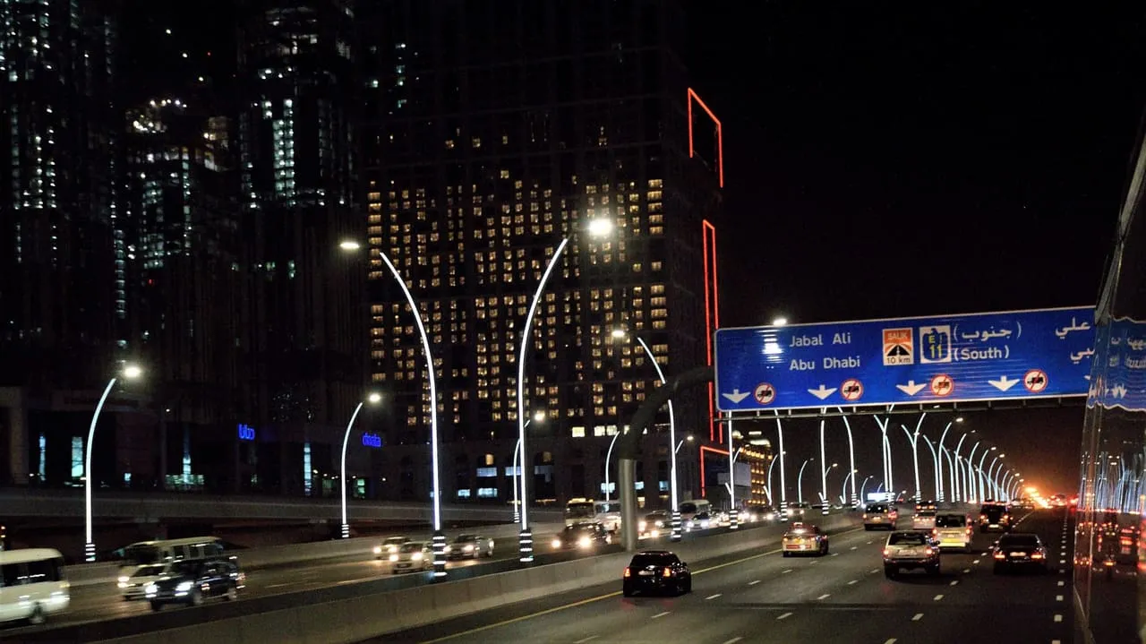 The E11 in Dubai at night, under an overhead sign for Jabal Ali and Abu Dhabi