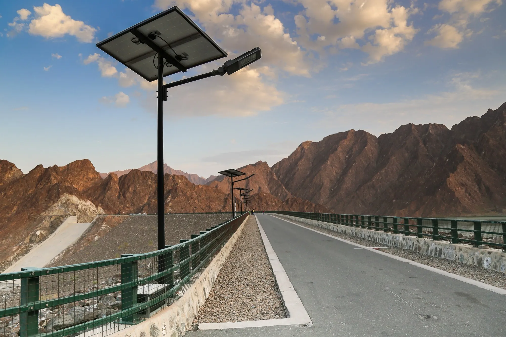The paved road across Hatta Dam with solar street lamps and the Hajar mountains