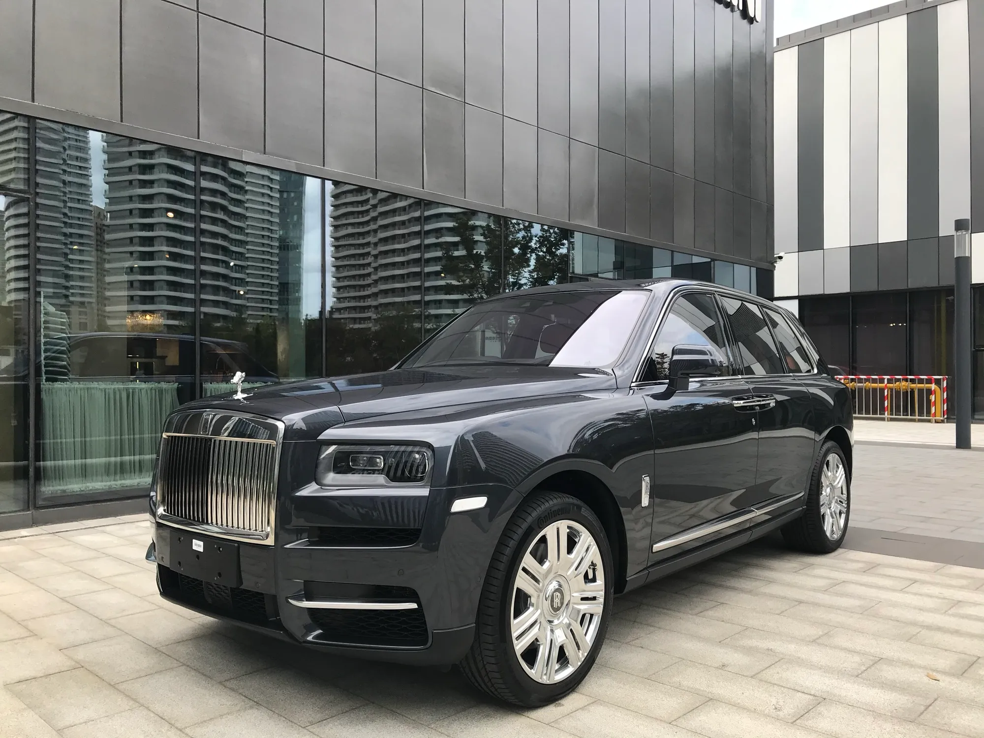 A black Rolls-Royce Cullinan SUV parked outside a glass-fronted building