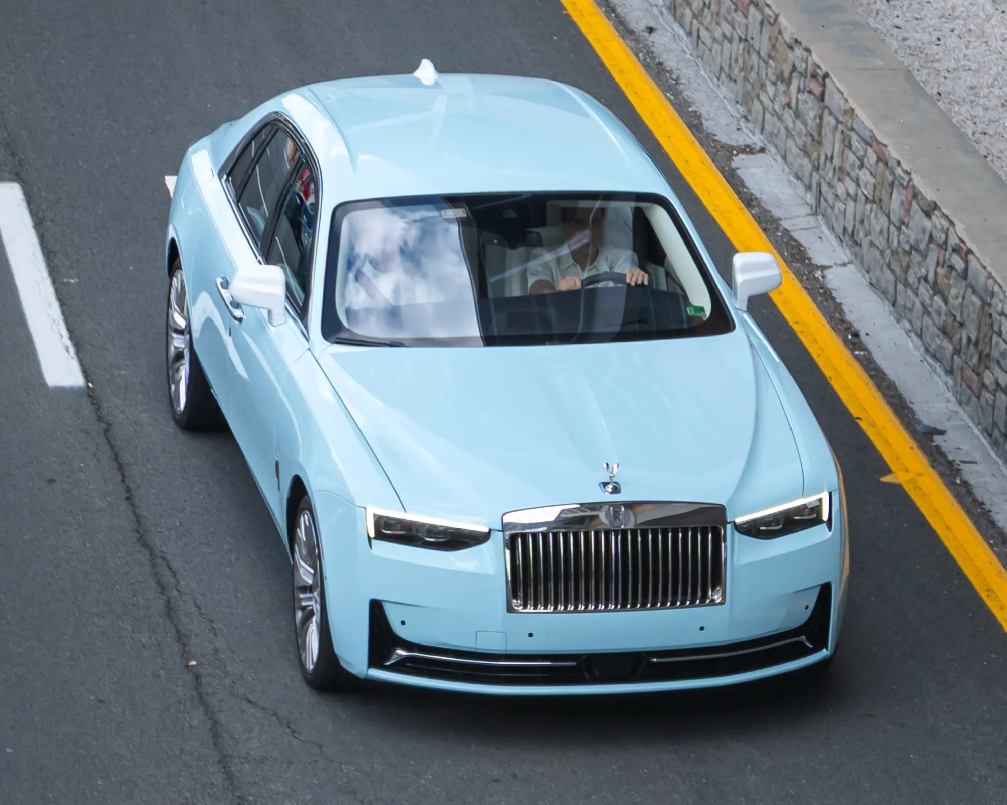 A pale blue Rolls-Royce Ghost seen from above, driving on a road