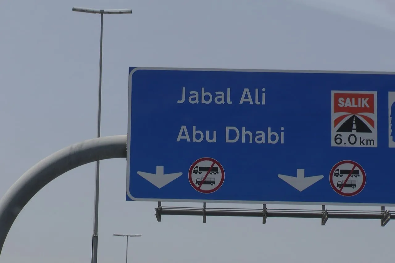 A blue road sign for Jabal Ali and Abu Dhabi warning of a Salik toll gate 6 km ahead