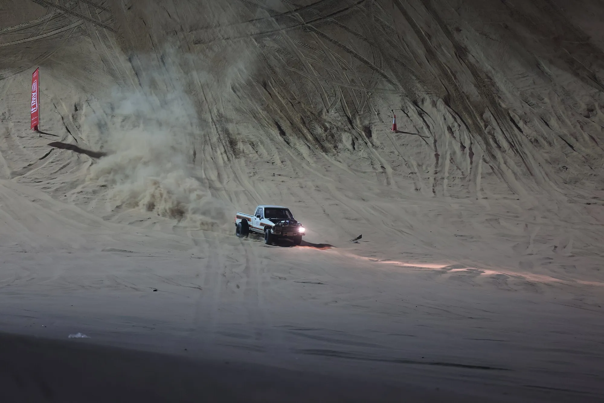 A pickup truck throwing up sand on a dune slope during a sand race at the Liwa International Festival 2022