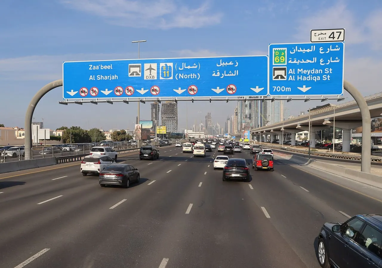 Traffic on Sheikh Zayed Road (E11) in Dubai under an overhead sign pointing to Al Sharjah and DXB
