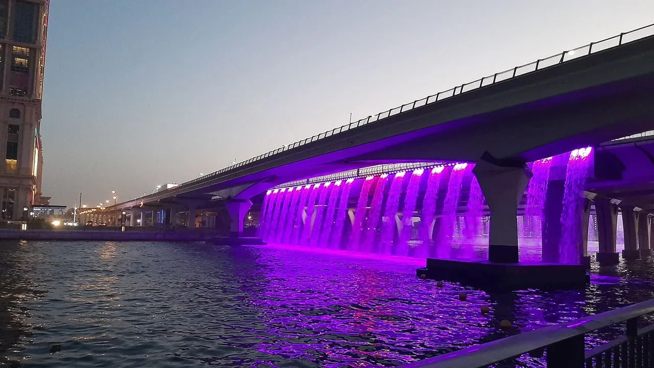 Lit waterfalls pouring from the Sheikh Zayed Road bridge into the Dubai Water Canal at dusk
