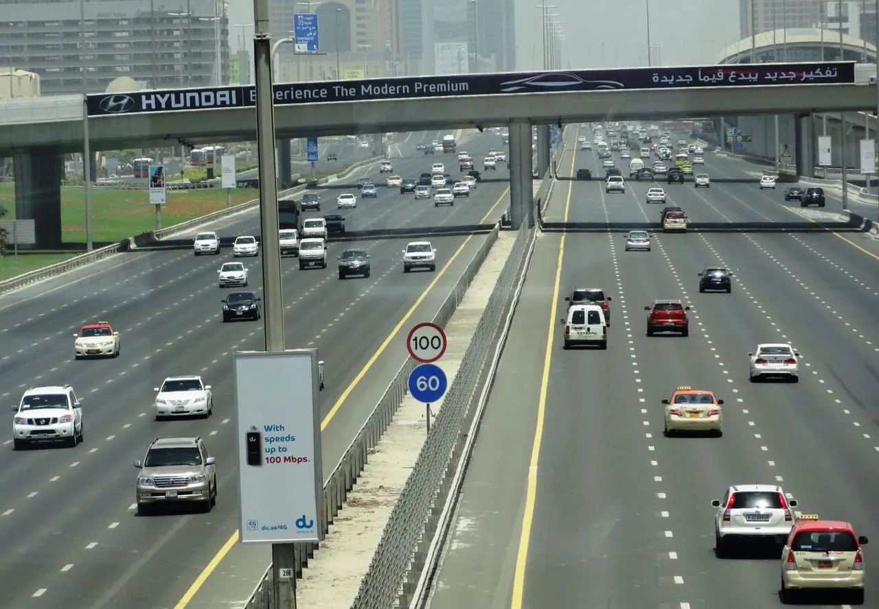 Cars and Dubai taxis on Sheikh Zayed Road, with a 100 km/h speed limit sign by the central barrier