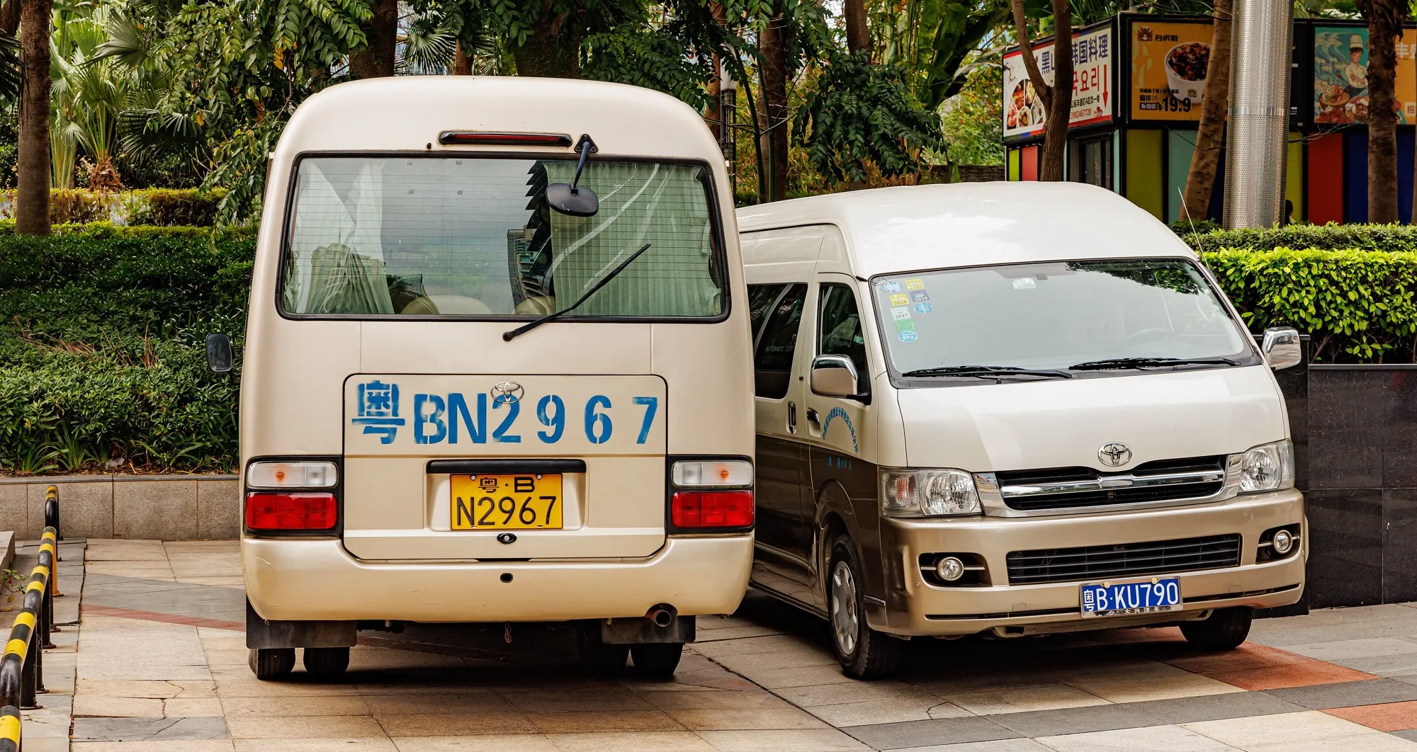 A Toyota Coaster seen from the back parked next to a Toyota Hiace, showing the difference in size