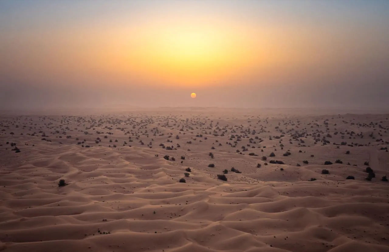 The sun rising through haze over the dunes of the Dubai Desert Conservation Reserve, seen from the air