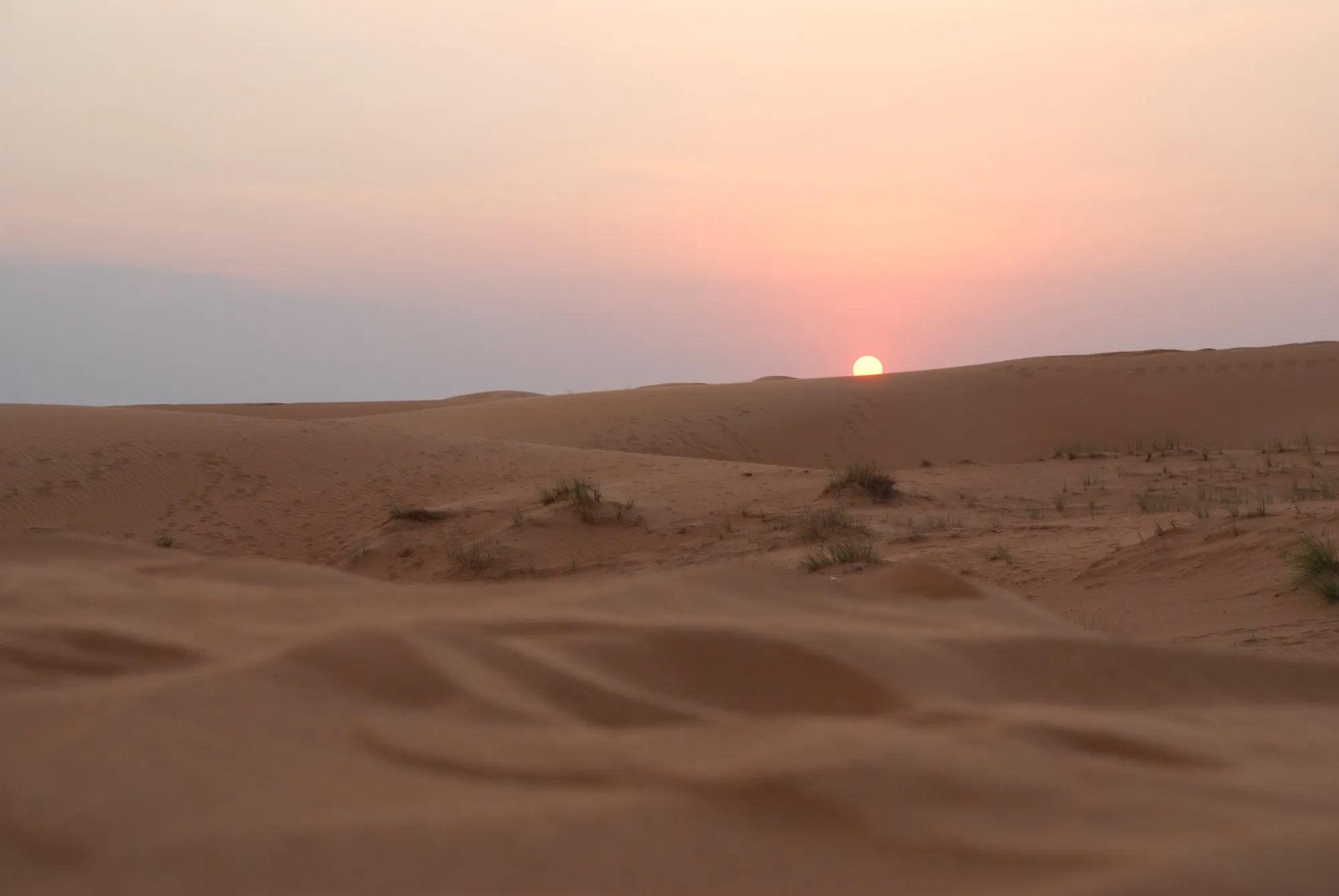 The sun setting behind low sand dunes in the desert outside Dubai