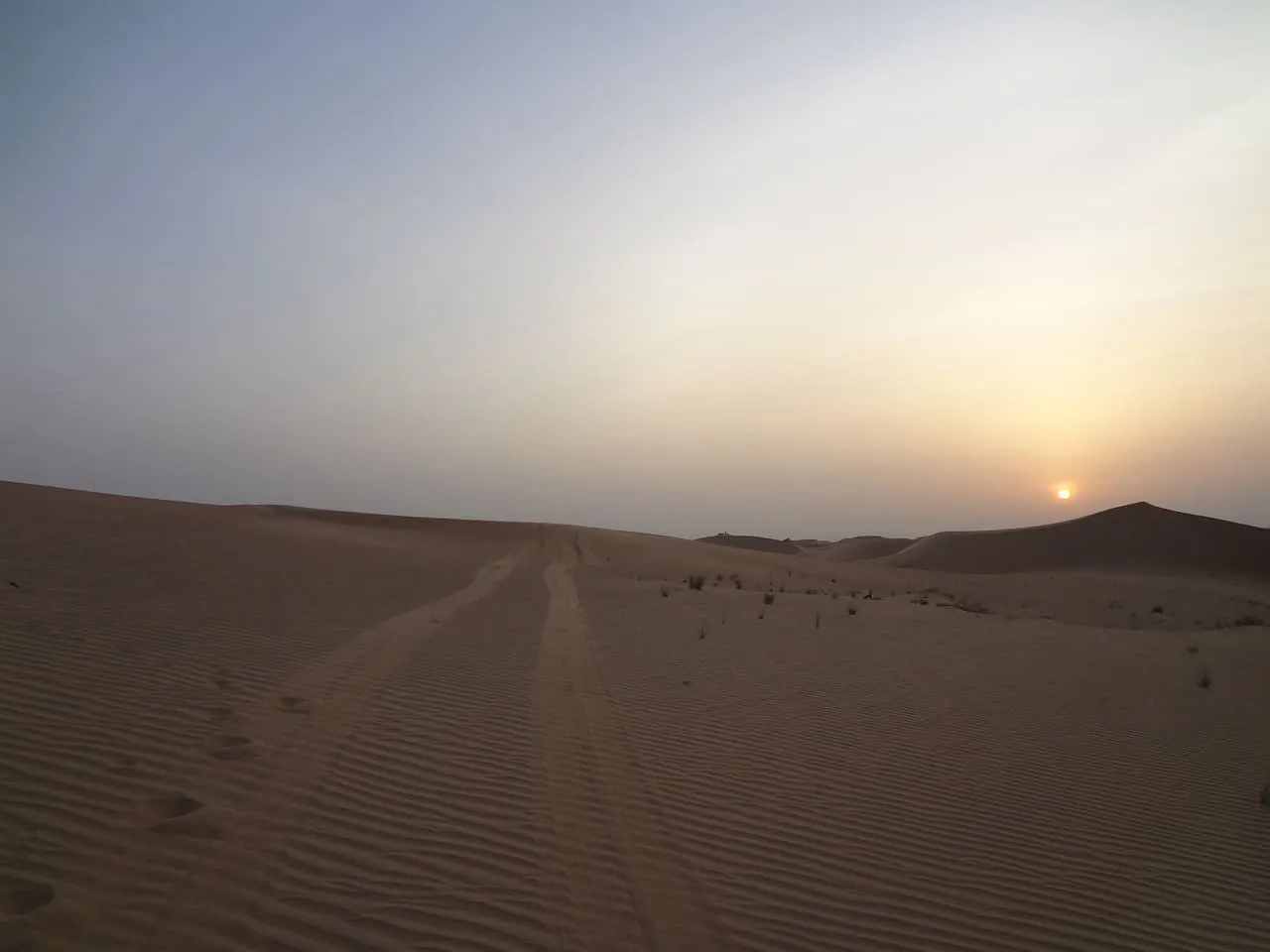 Tyre tracks running across the sand towards the setting sun in the Abu Dhabi desert