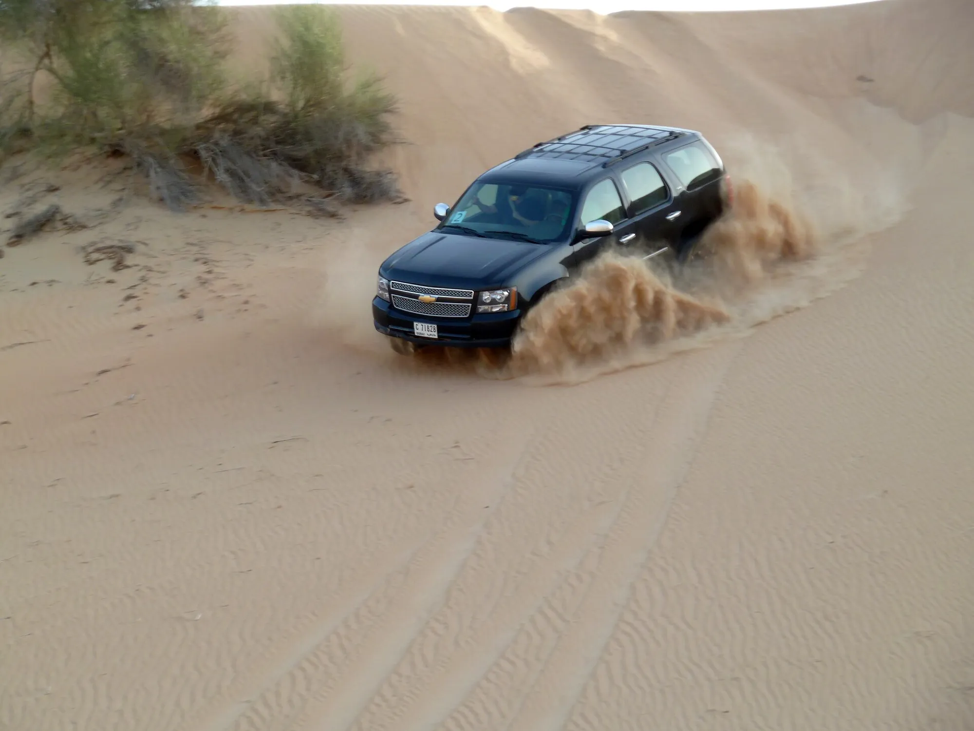 A black SUV throwing up sand as it drives down a dune in the Dubai desert