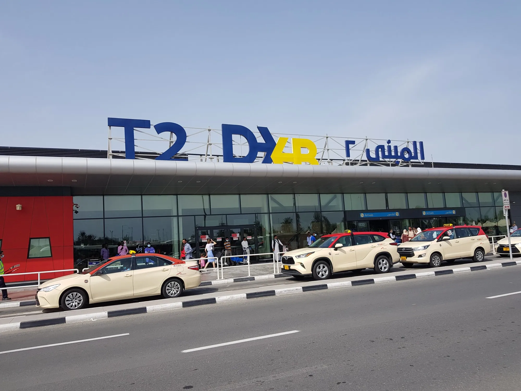Dubai Taxi cars in front of the arrivals entrance under the T2 sign at Dubai International Terminal 2