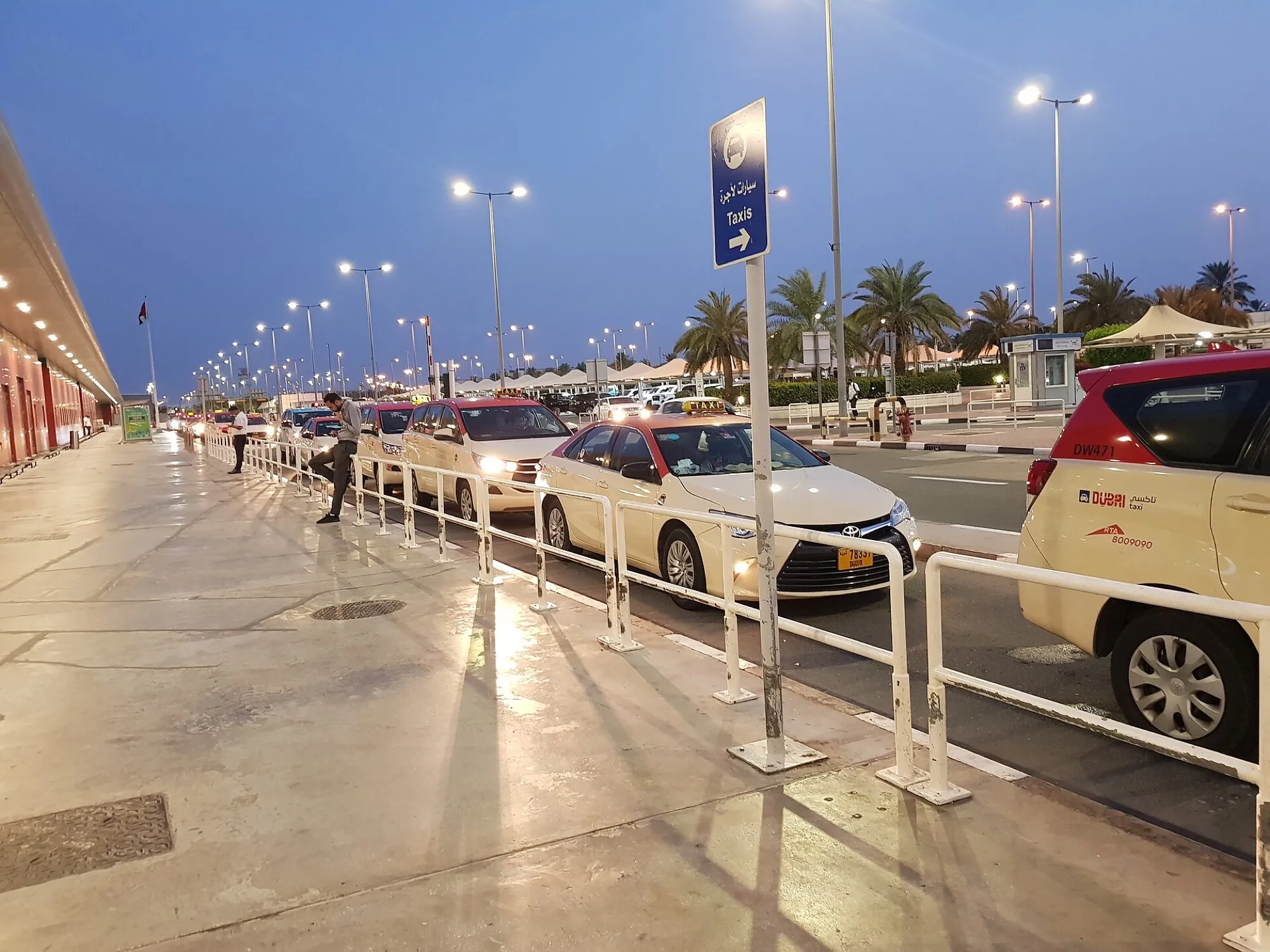 Dubai Taxi cars queuing at the rank outside Terminal 2 at dusk, under a blue Taxis sign