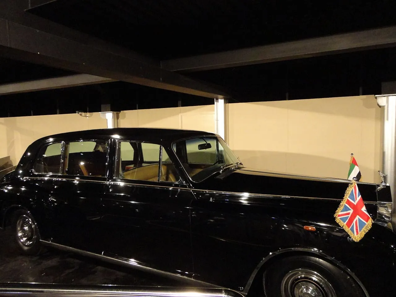 A black vintage Rolls-Royce Phantom limousine with the UAE flag and the Union Flag on its front wings, on display at the Emirates National Auto Museum in the UAE